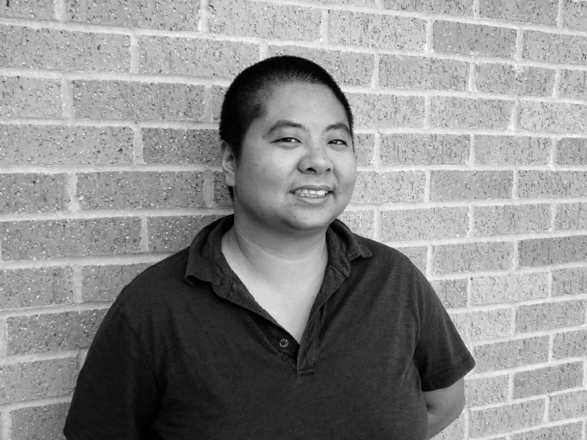 A black and white photo of Ching-In Chen, a genderqueer Asian American standing against a brick wall.