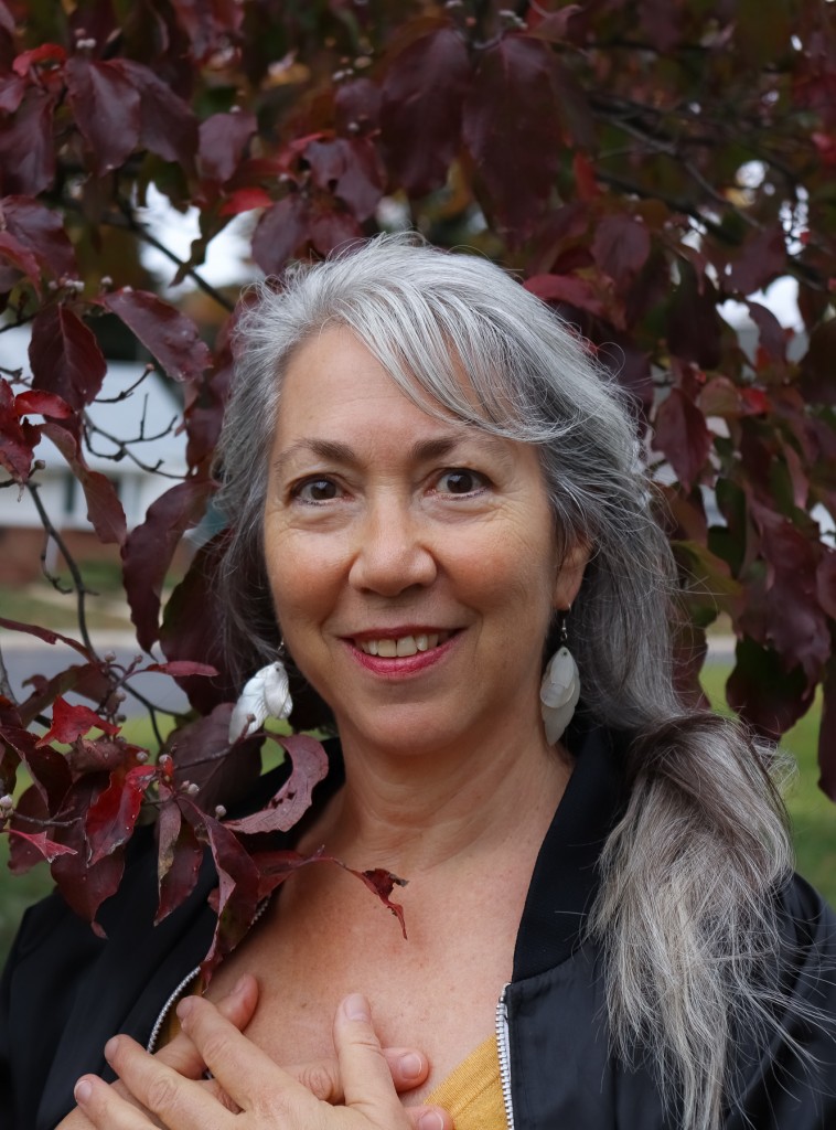 Diana Tokaji with silver hair in front of wine-colored leaves.