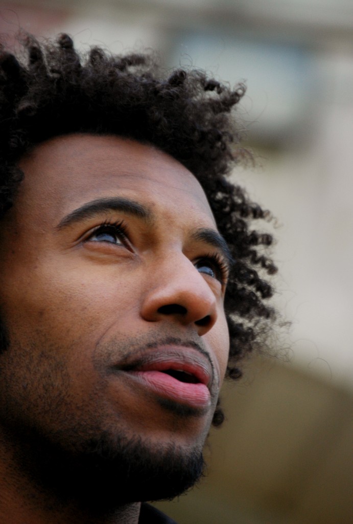 Profile photo of Kyle Dargan (a brown-skinned Black-American man with curly afro) looking up at the sky