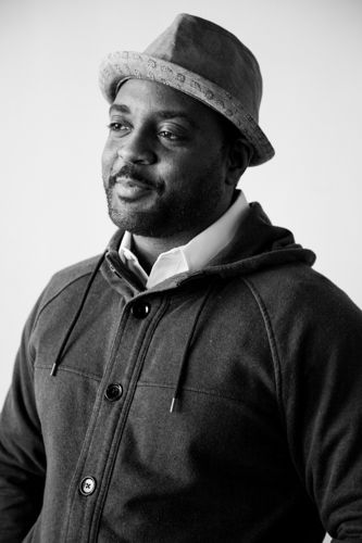 Black and white photo of Reginald Dwayne Betts in hat and a jacket with a slight smile