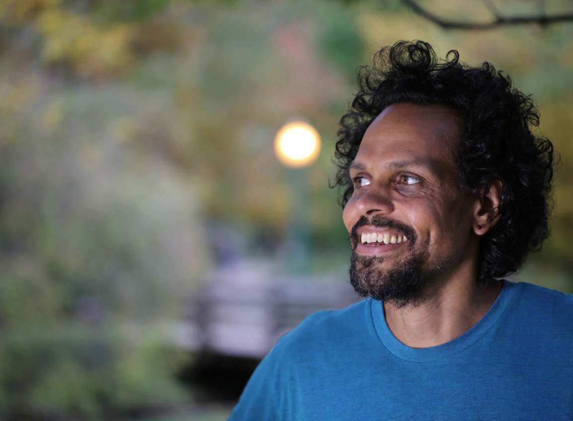 Photo of Ross Gay outside in blue shirt smiling